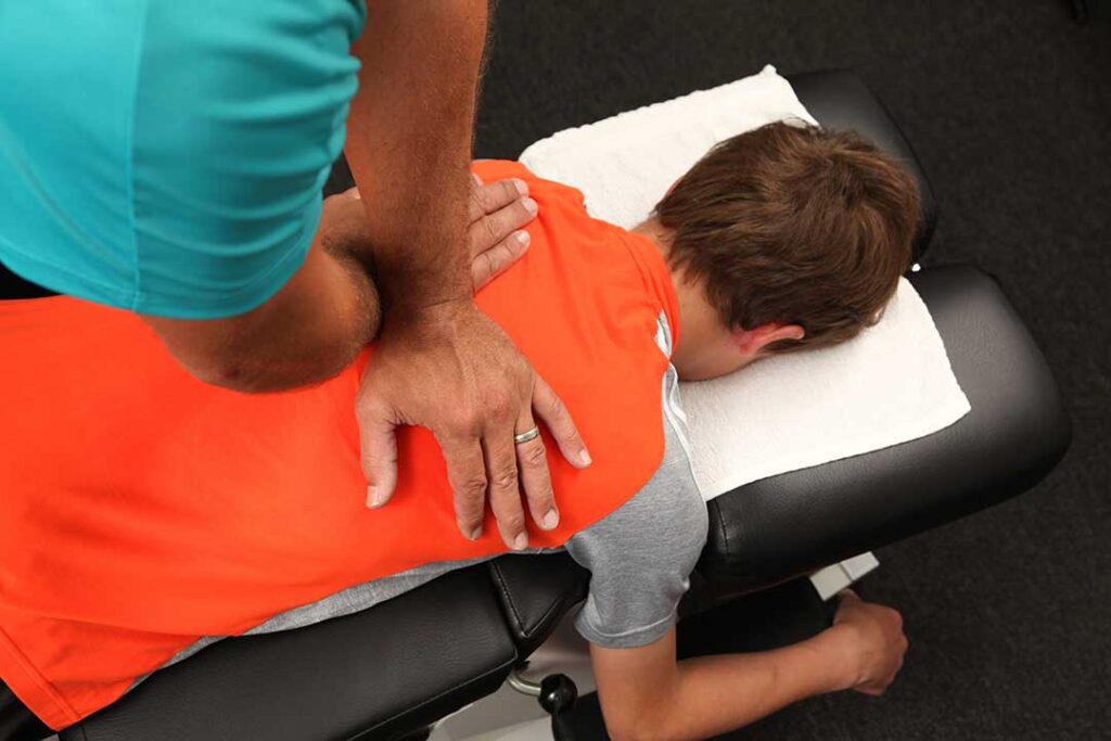 A chiropractor gently assessing an athlete’s back and shoulders in a clinical setting.