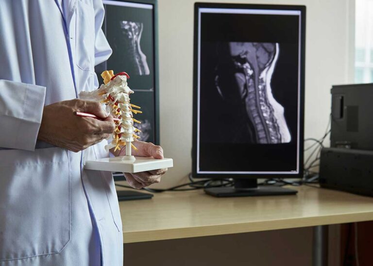 A person seated at a desk in a home setting, sitting upright with a neutral spine at a computer.