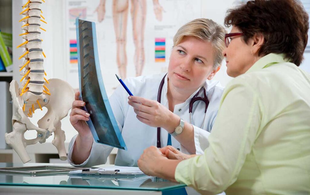 A patient in casual clothes talking with a chiropractor in a bright, comfortable exam room.